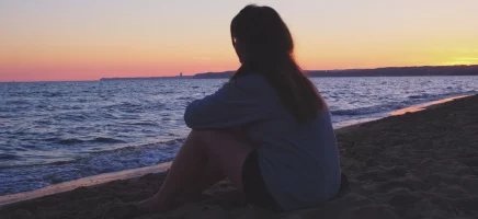 A girl sitting quietly on the beach, looking out at the calm ocean horizon.
